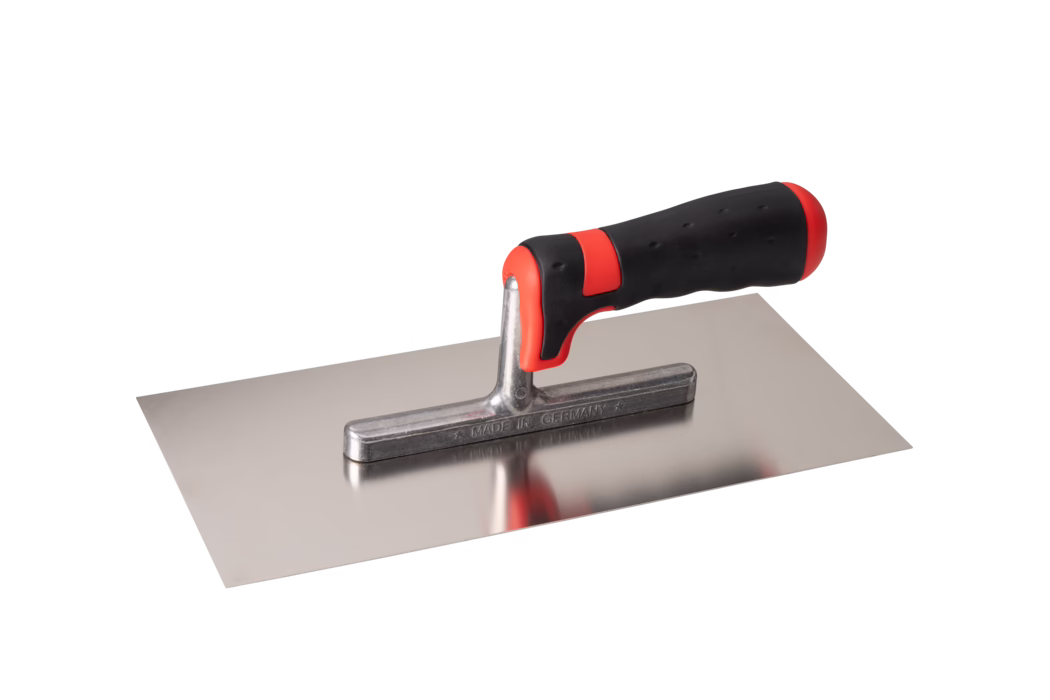 Rechteckige Glättkelle aus Edelstahl mit glatter, flacher Klinge und kurzem Metallstiel, der einen ergonomisch geformten schwarz-roten Softgriff trägt. Die polierte Klinge ist spiegelnd und zeigt eine leichte Reflexion des Griffes; der Metallstiel ist mit der Aufschrift MADE IN GERMANY versehen. Der Griff hat rote Akzente vorne und hinten sowie eine strukturierte Gummierung für sicheren Halt. Das Werkzeug ist freigestellt vor weißem Hintergrund aus einem leicht erhöhten Seitenwinkel fotografiert. Geeignet zum Auftragen und Glätten von Mörtel, Putz oder Spachtelmasse.